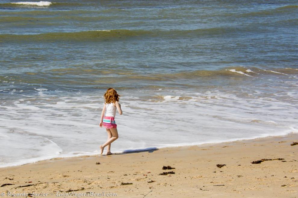 Imagem de uma menina andando na beira do mar na Praia de Santo André.